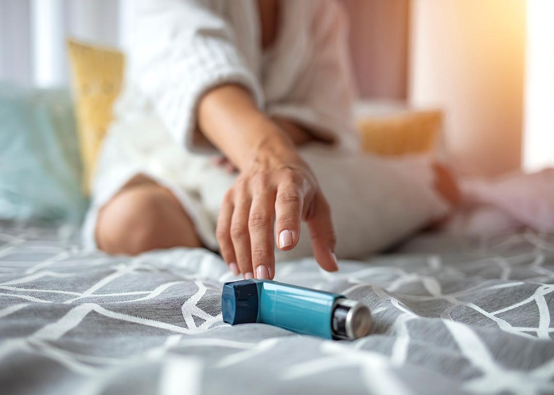 Woman sitting on a bed reaching for her inhaler.