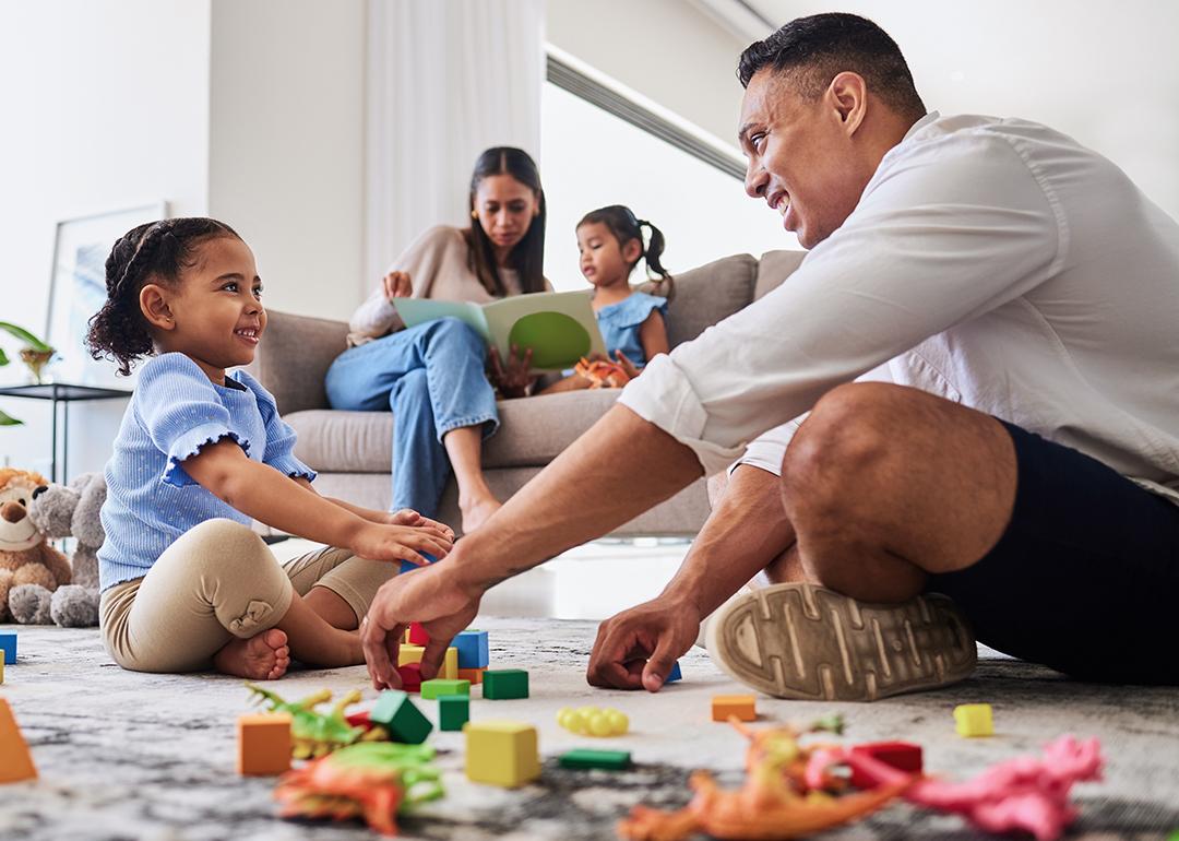Parents playing with and reading a book to their young daughters at home.