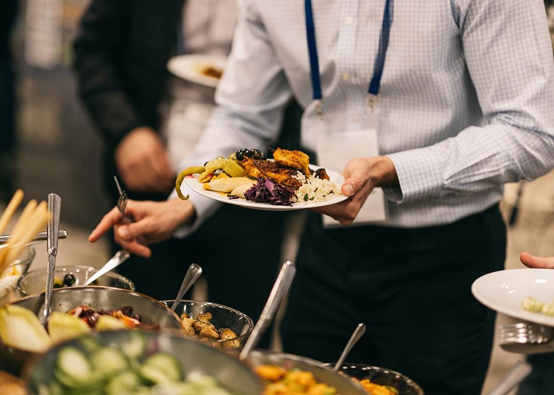 An employee holding up a plate of Mediterranean food from a catering event.