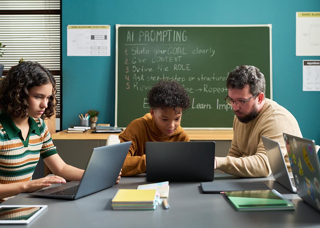 A male teacher guiding students in a classroom in using AI.