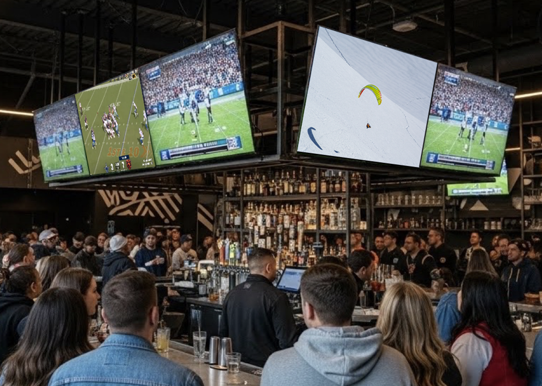 People surround a bar where multiple TVs stream a football match.