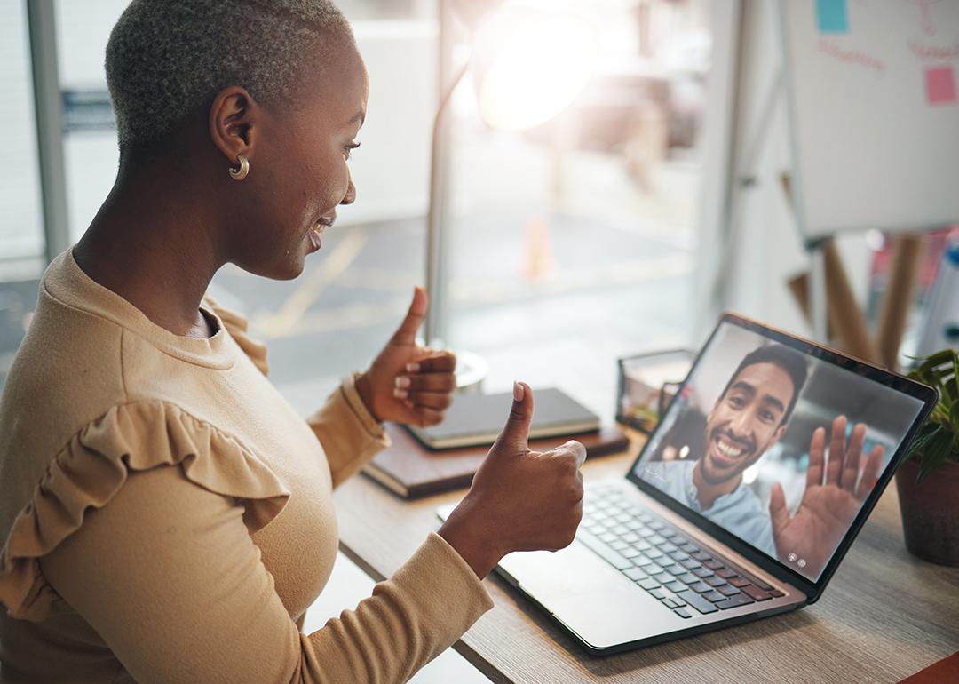 A black woman in an office happily putting two thumbs up during a video call.