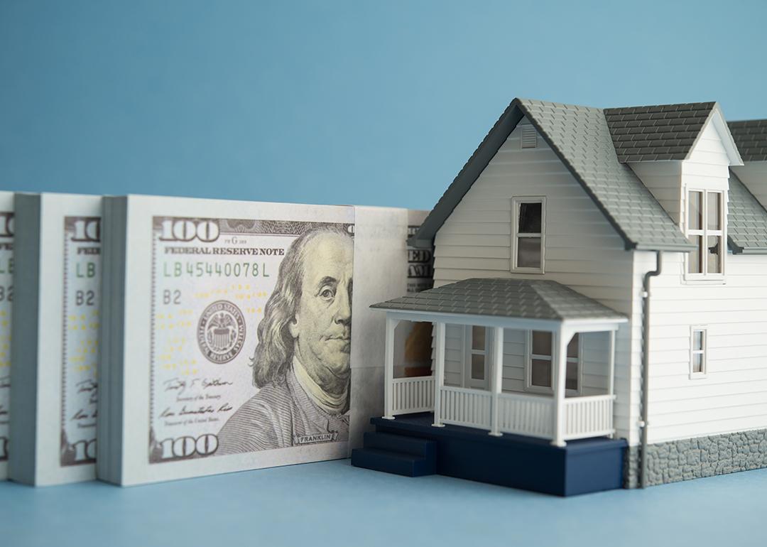 A house miniature and U.S. dollar banknotes in a blue background.