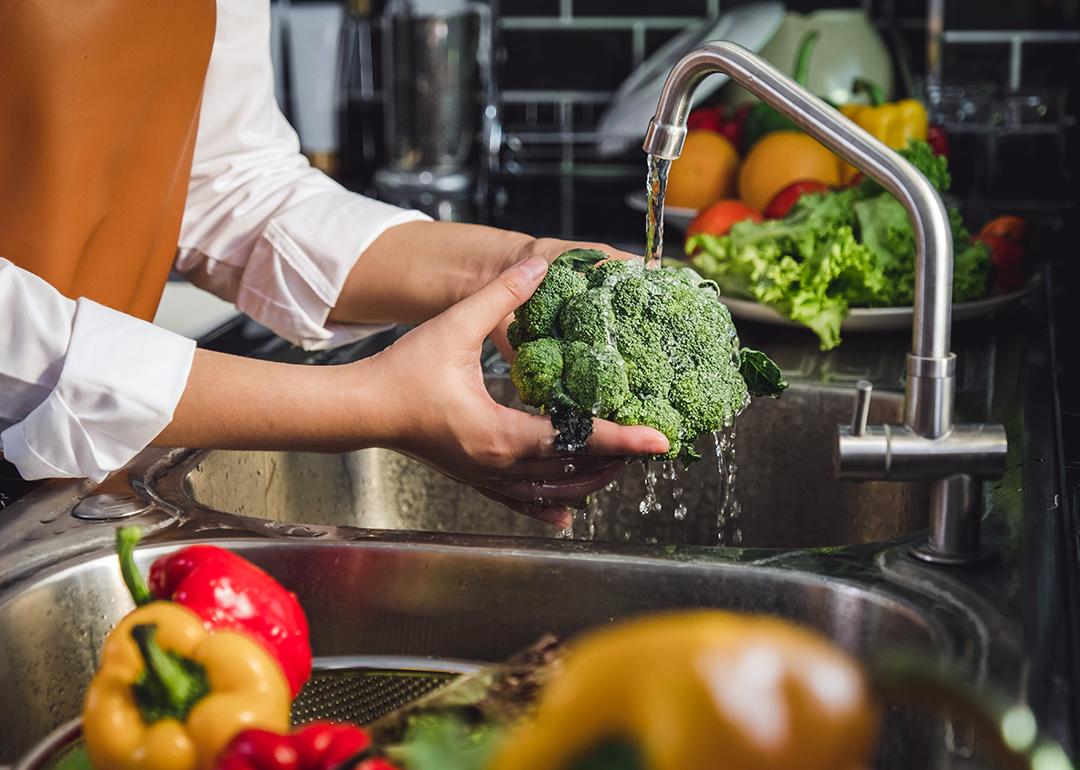 Person washing fresh vegetables over the sink.