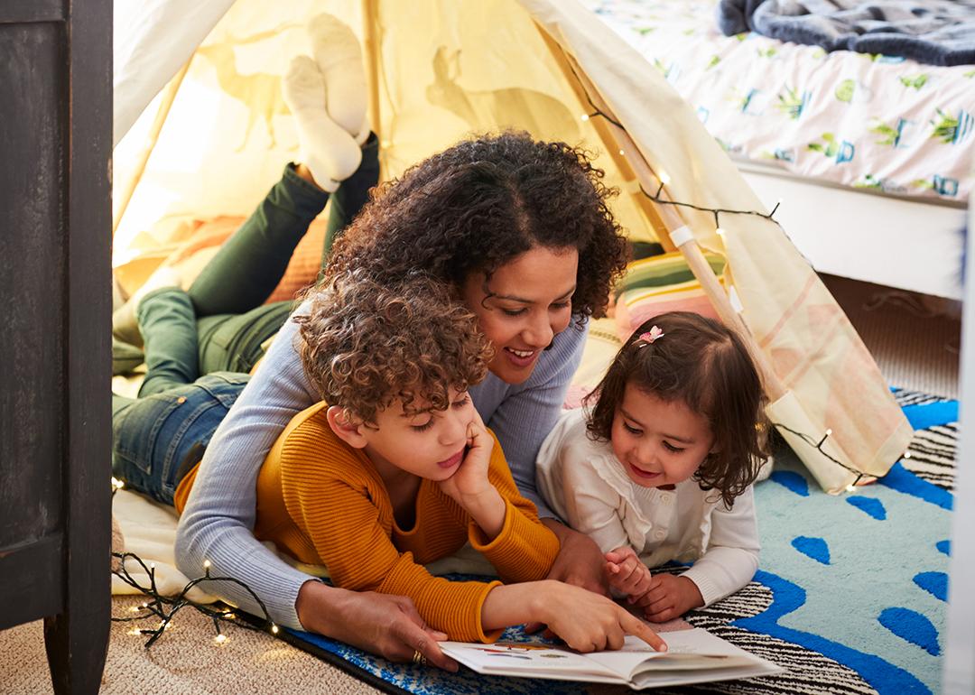 A mother reading a book to his young son and daughter on the floor.
