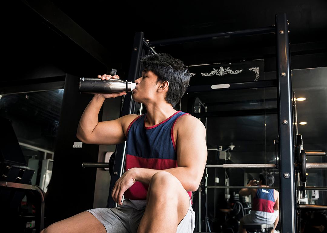 A young, fit man drinking water inside a gym.