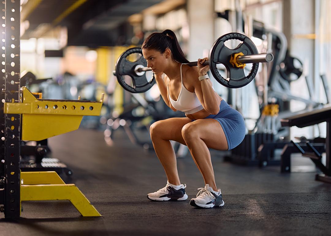 An athletic woman squatting with a barbell in a gym.