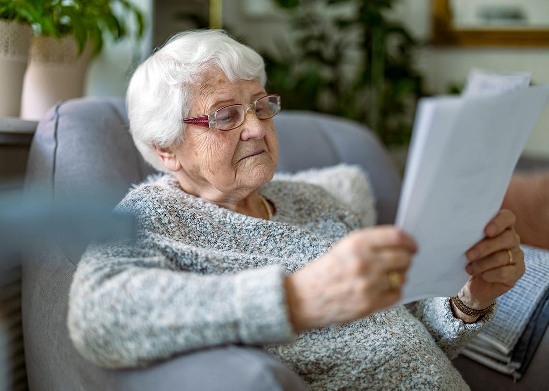 A senior woman reading documents while sitting in an armchair in a living room.