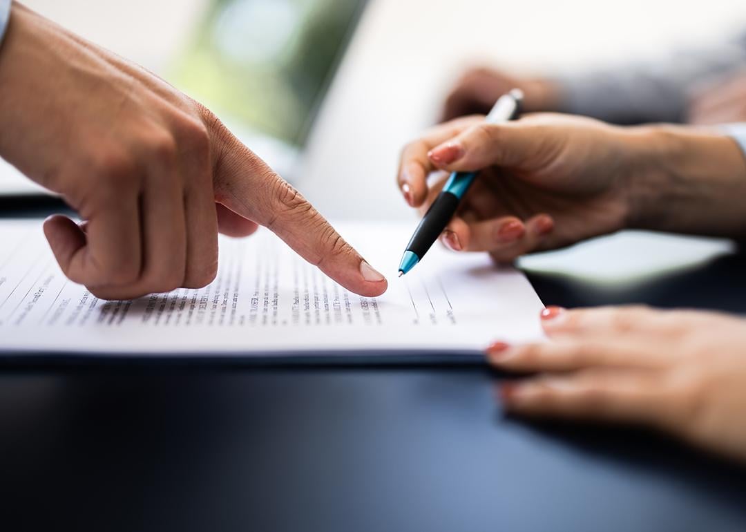A pointing finger guiding the other person where to sign in a document.