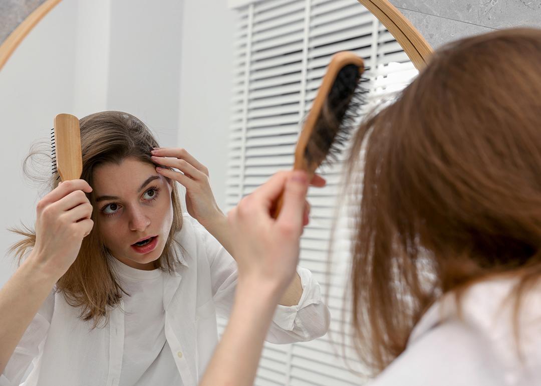 A person checking her hair while facing a mirror in a bathroom.