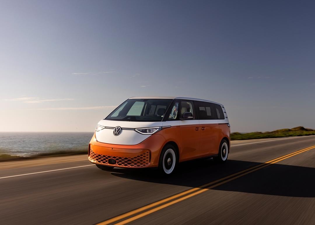 Candy White over Energetic Orange 2025 Volkswagen ID Buzz driving on road next to ocean.