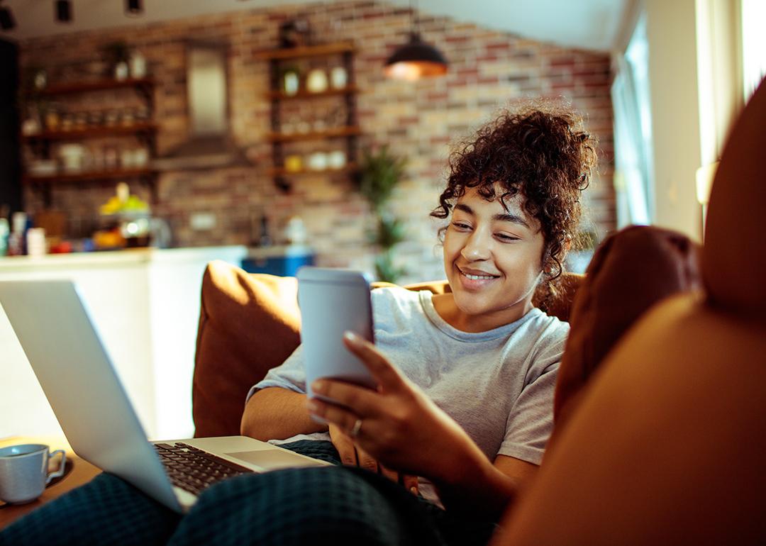 A young woman at home smiling at her phone while relaxing on a couch.