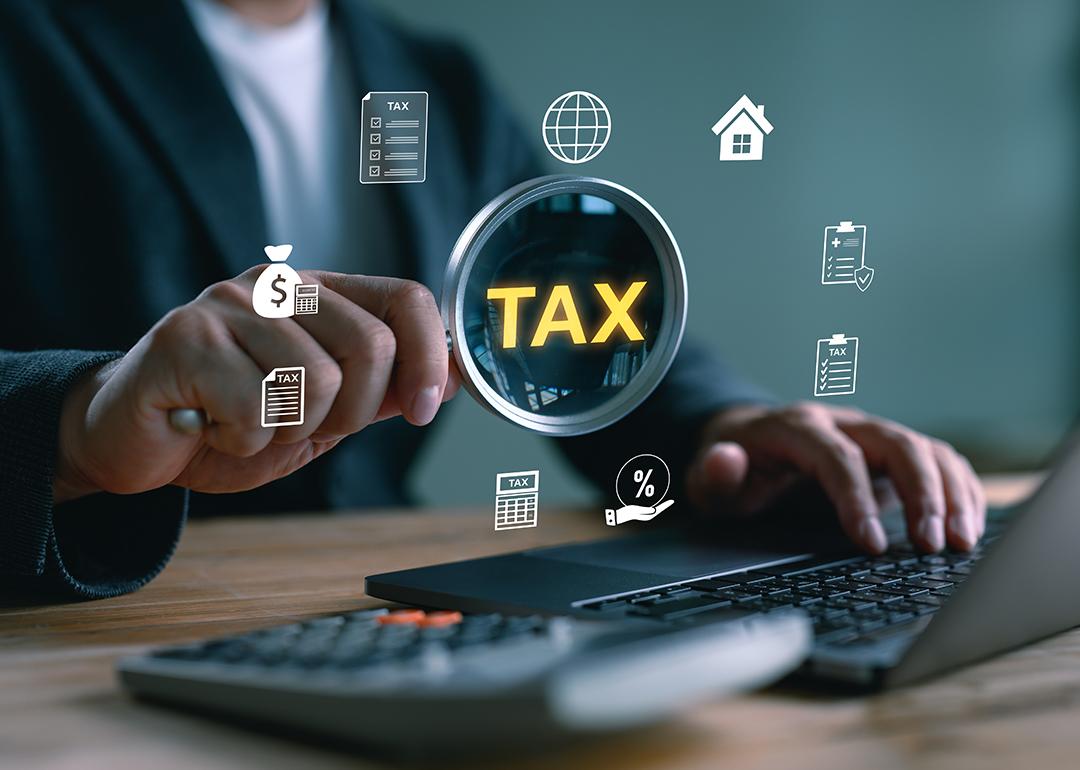 'Tax' and related graphics illustrated over a magnifying glass focusing on a computer as a concept of tax filing.