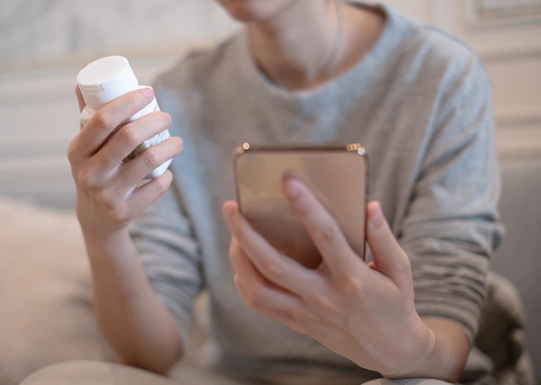 A person holding a vitamin bottle while checking prescription instructions in a smartphone.