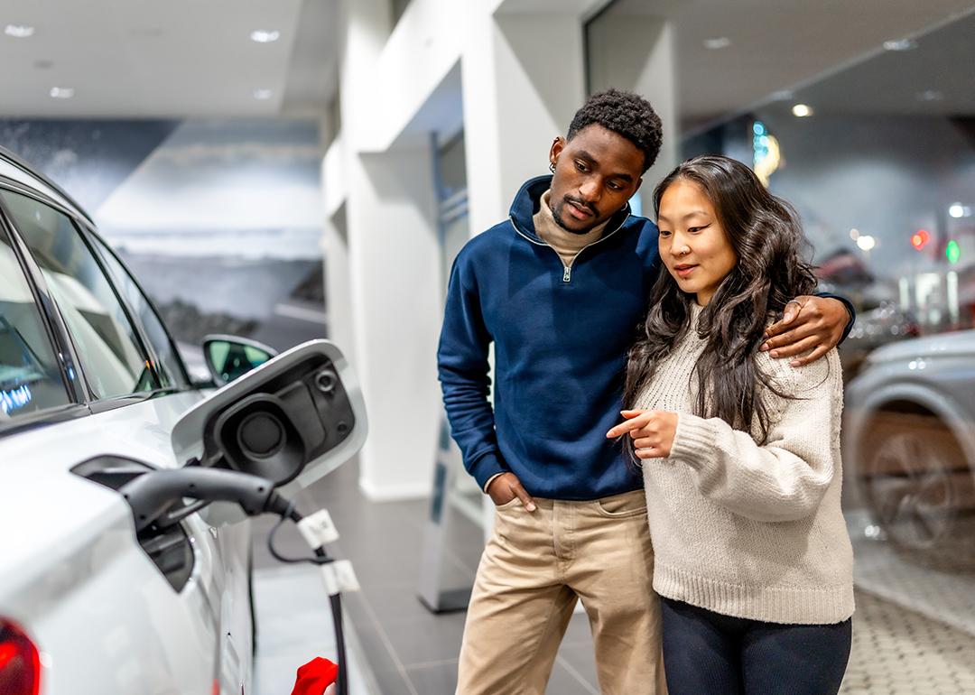 A multiethnic couple examining the charging port of an electric vehicle at a car dealership.