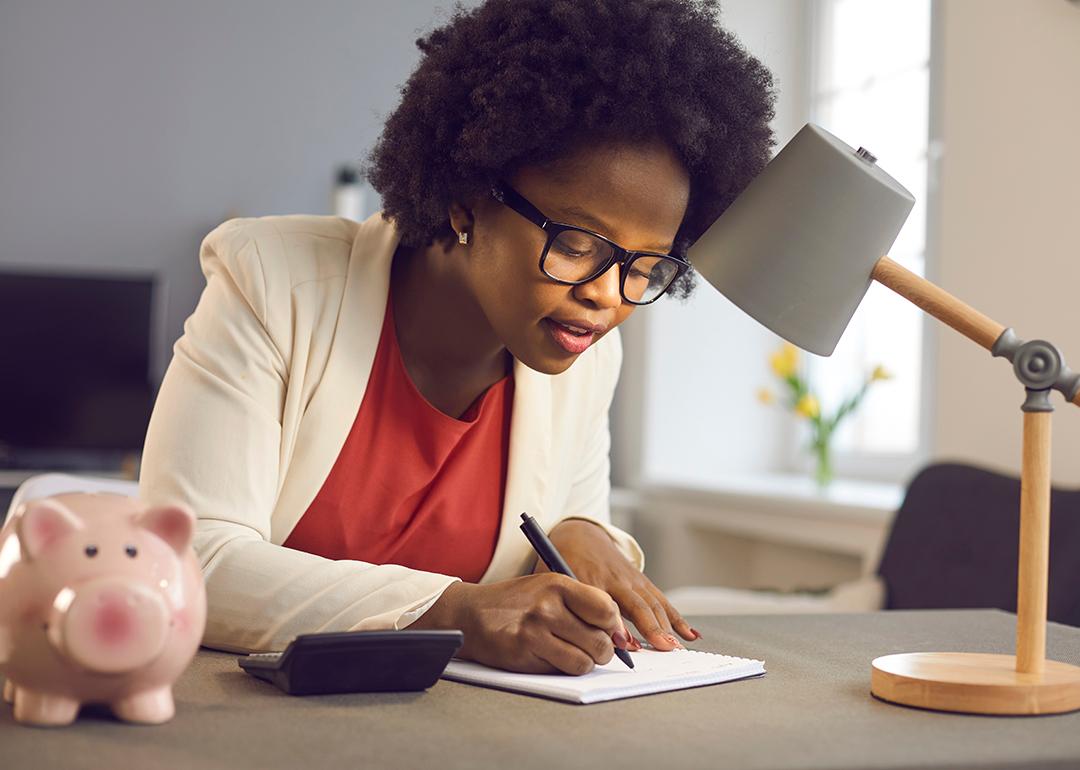 A black businesswoman writing notes beside a piggy bank as a concept of budgeting.