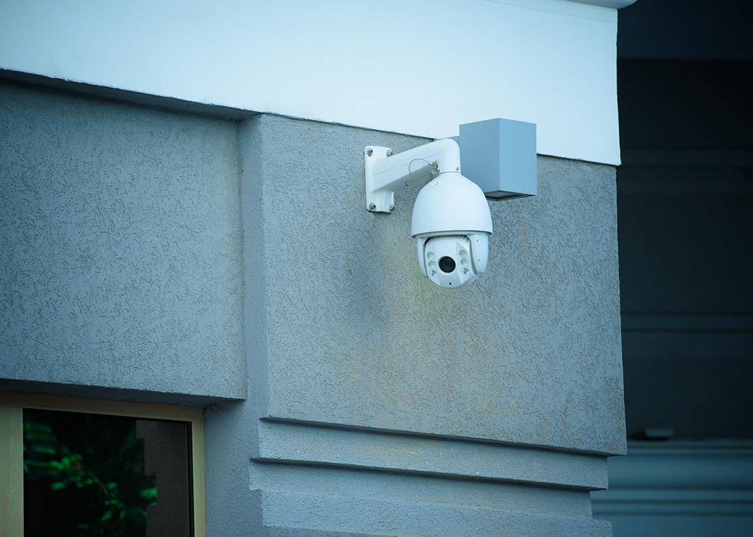 A view of a security camera on the facade of a gray building.