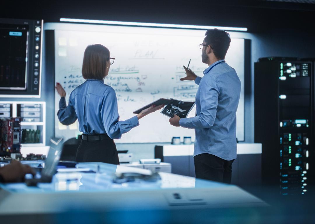 A team of two professional engineers using a digital tablet to discuss a manufacturing plan.