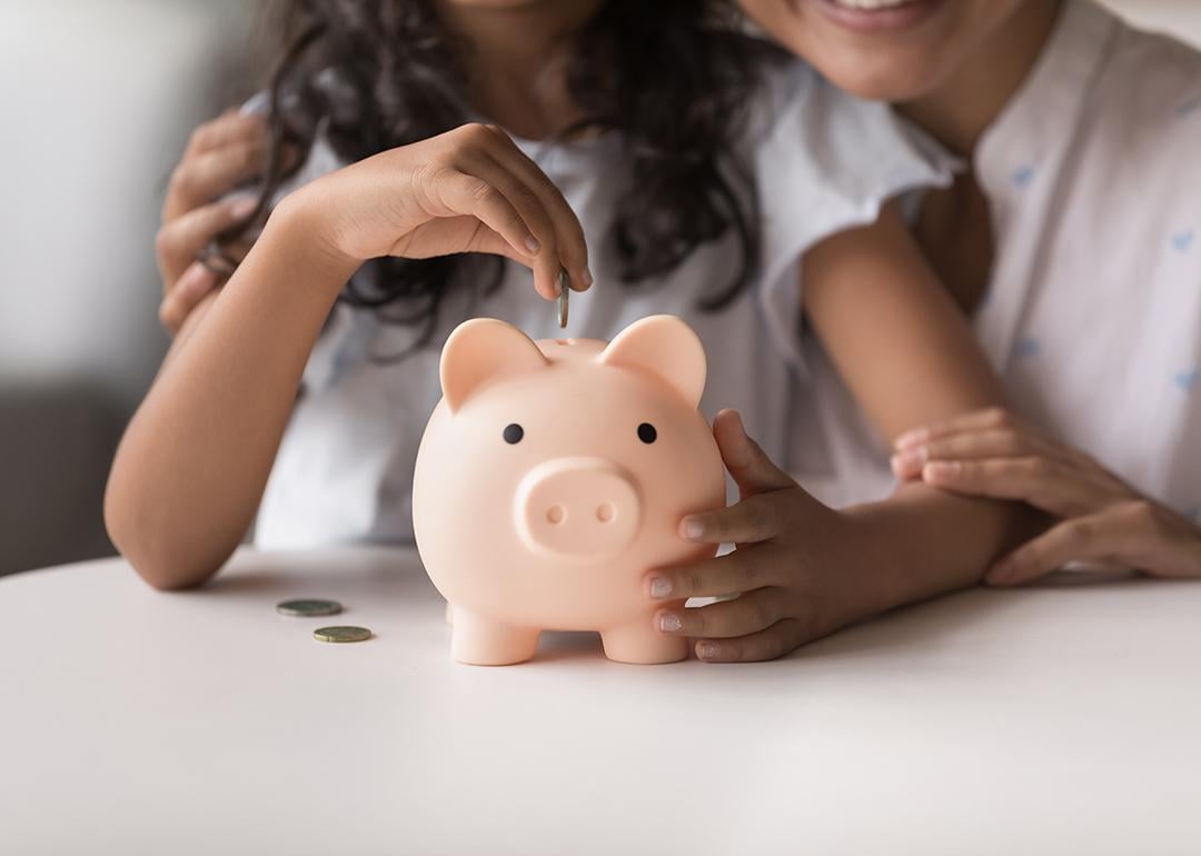 Mother helps daughter put coins in a piggy bank.