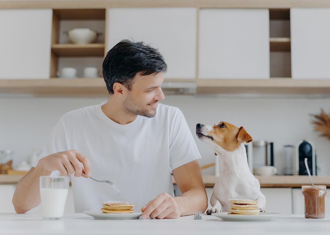Man at home eating pancakes with his dog.