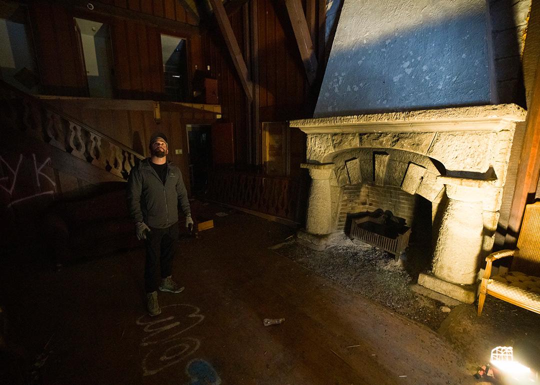Cameron Jensen standing inside one of his newly acquired buildings in Logan Canyon in front a fireplace illuminated by a floor lamp.