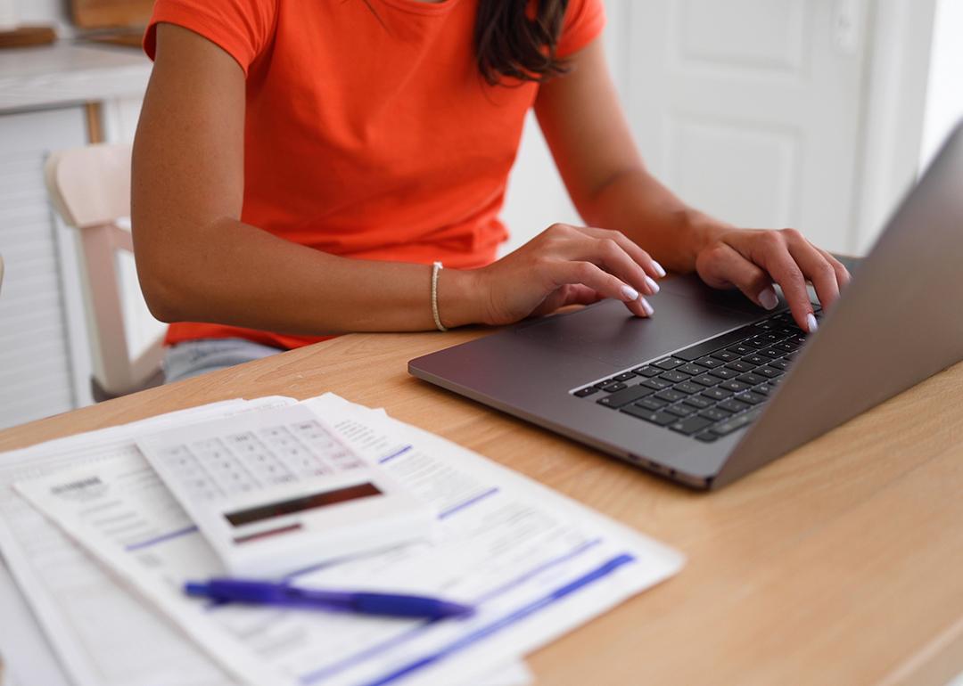 A woman organizing finances at home using a laptop and calculator over documents.