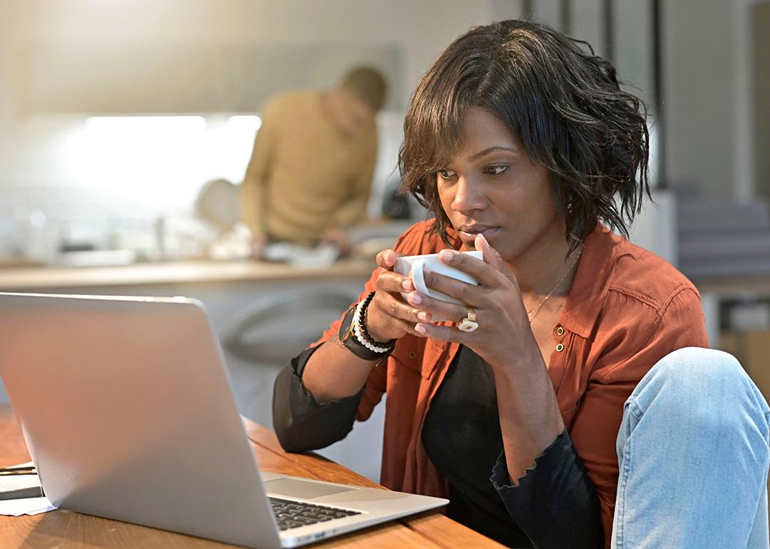 A black woman working from home and sipping a cup of coffee.