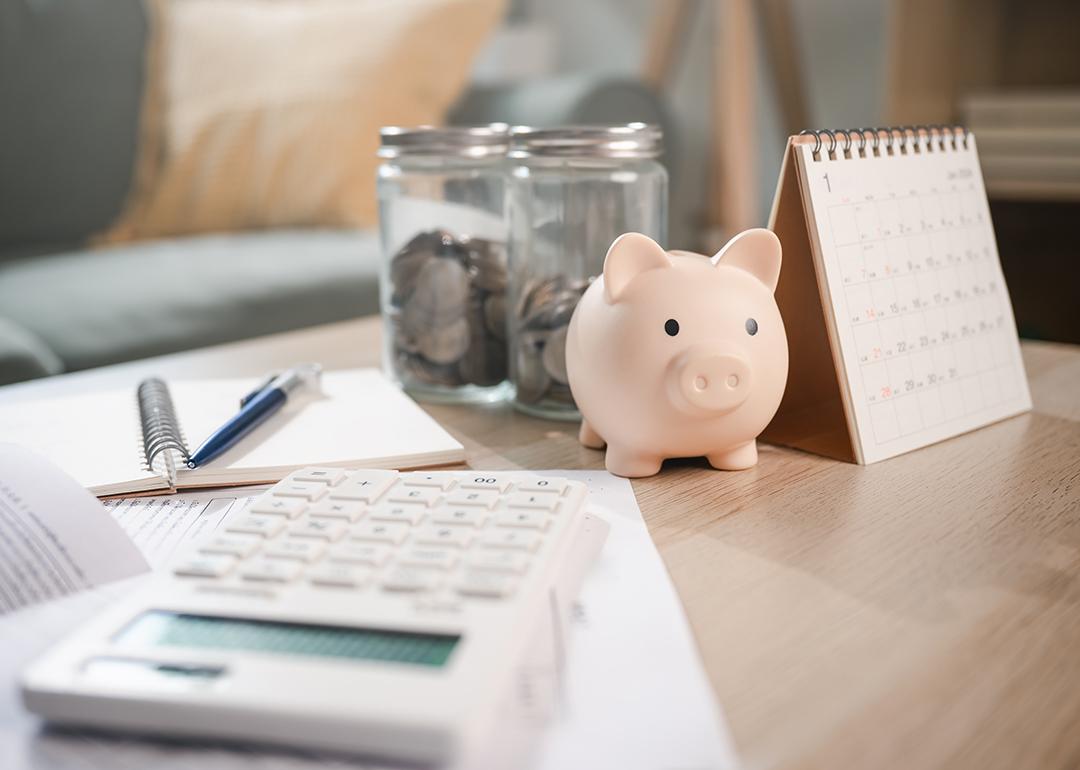 A piggy bank sits on a table with a calculator and a calendar.