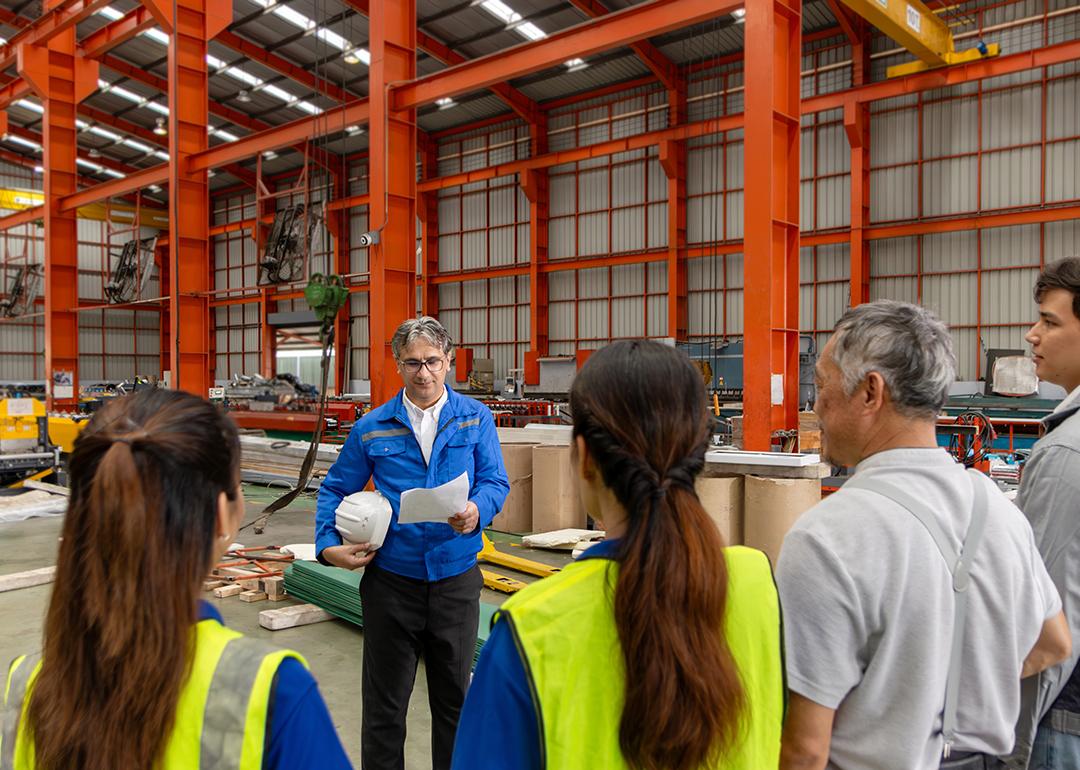 A supervisor leads his team for a briefing inside a manufacturing factory.