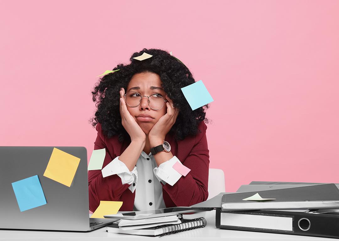 A young woman with sticky notes taped around her looking stressed at work.