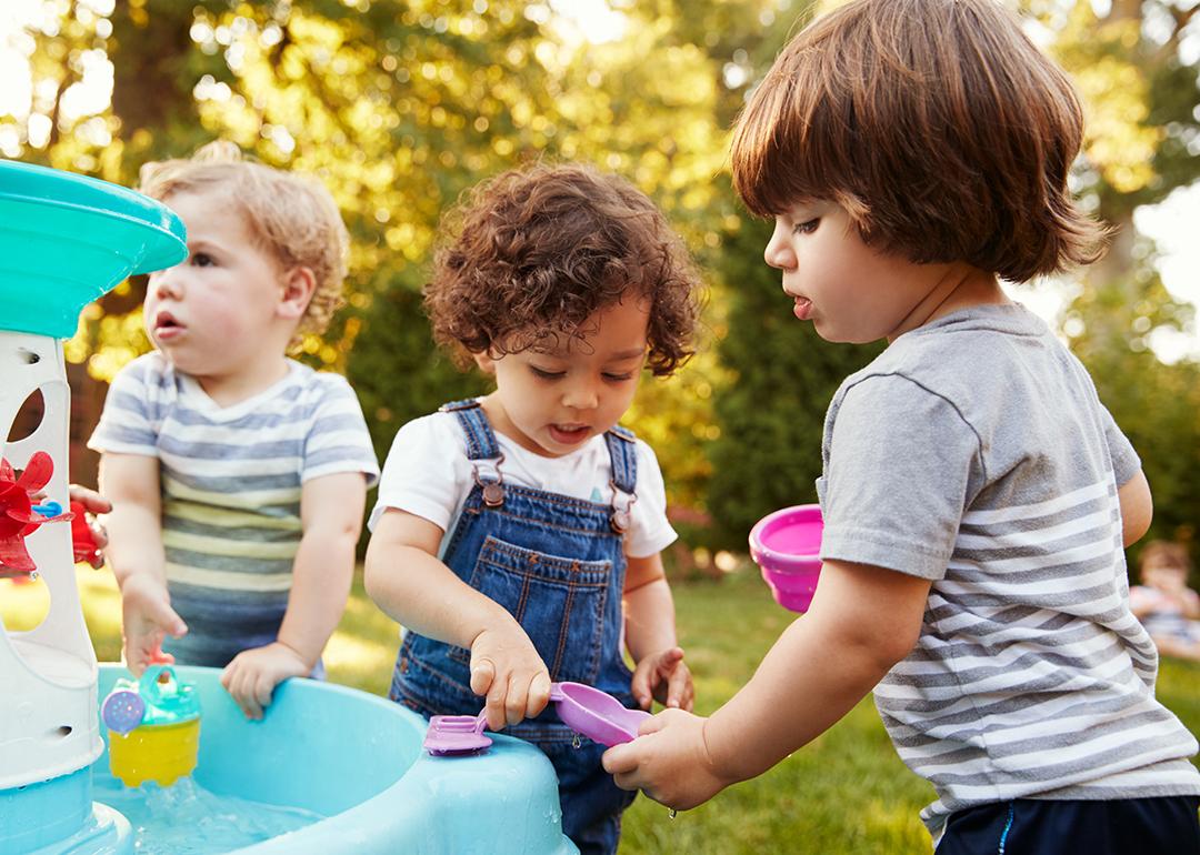 Three little children playing around a water table in a garden.