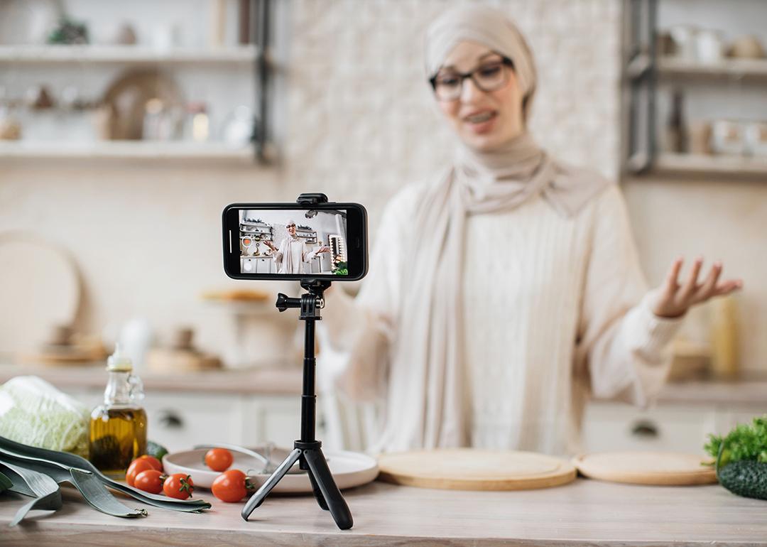 A young woman recording a video for her dieting and food blog using a smartphone on a tripod.