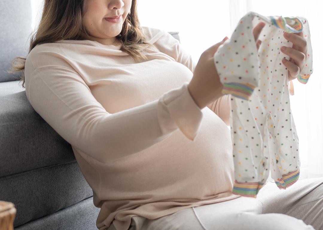 A pregnant woman checking on new baby clothes at home. 
