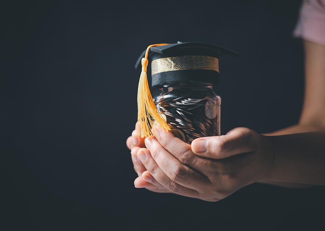 Person holding a jar of coins with a graduation cap as a concept of educational planning.