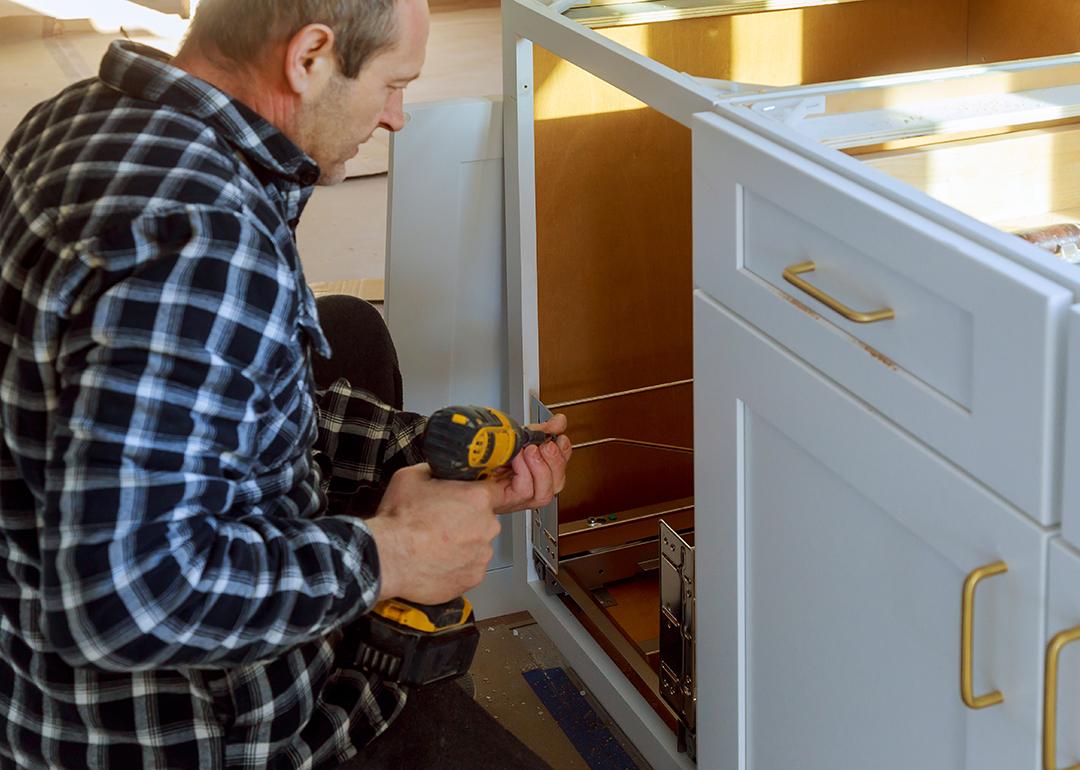 A woodworker installing a drawer for a garbage bin in a kitchen.
