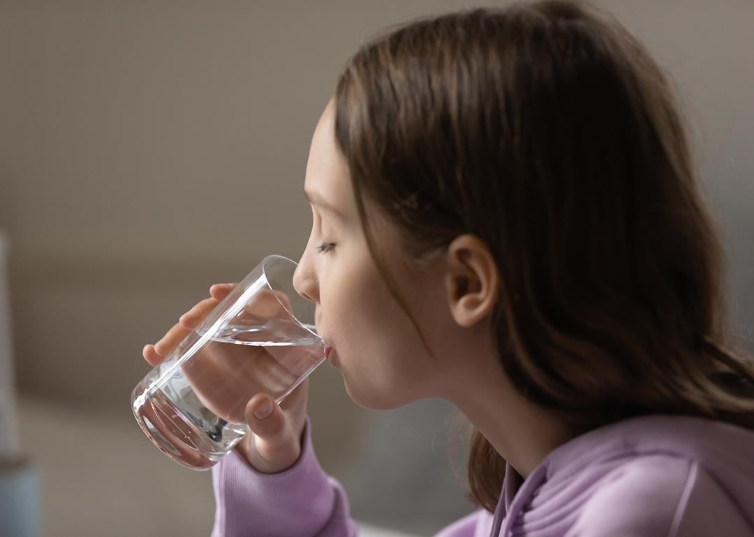 A young dehydrated teenage girl drinking a glass of water.