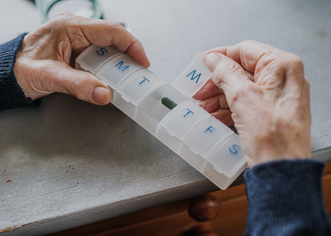 An elderly person arranging medicine in a pill box for the week.