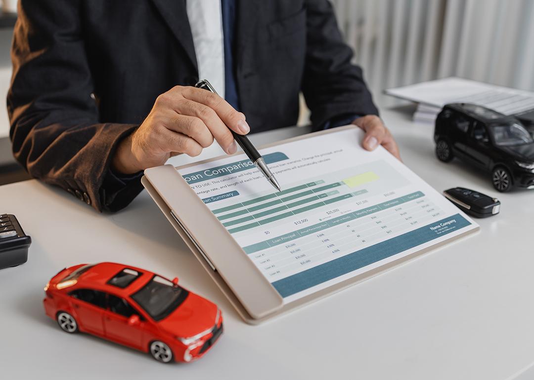 A loan officer showing a car loan comparison document to a client.