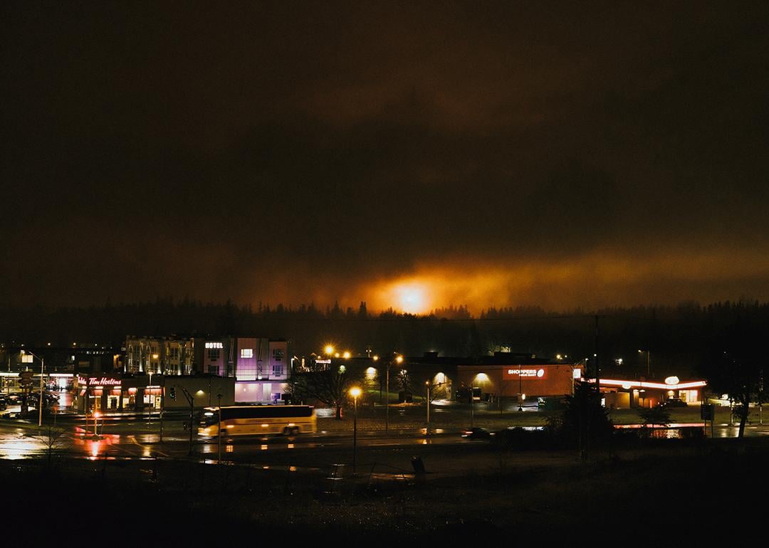 A large flame from a gas flare in Kitimat is visible at night, with the city streets visible in the foreground.