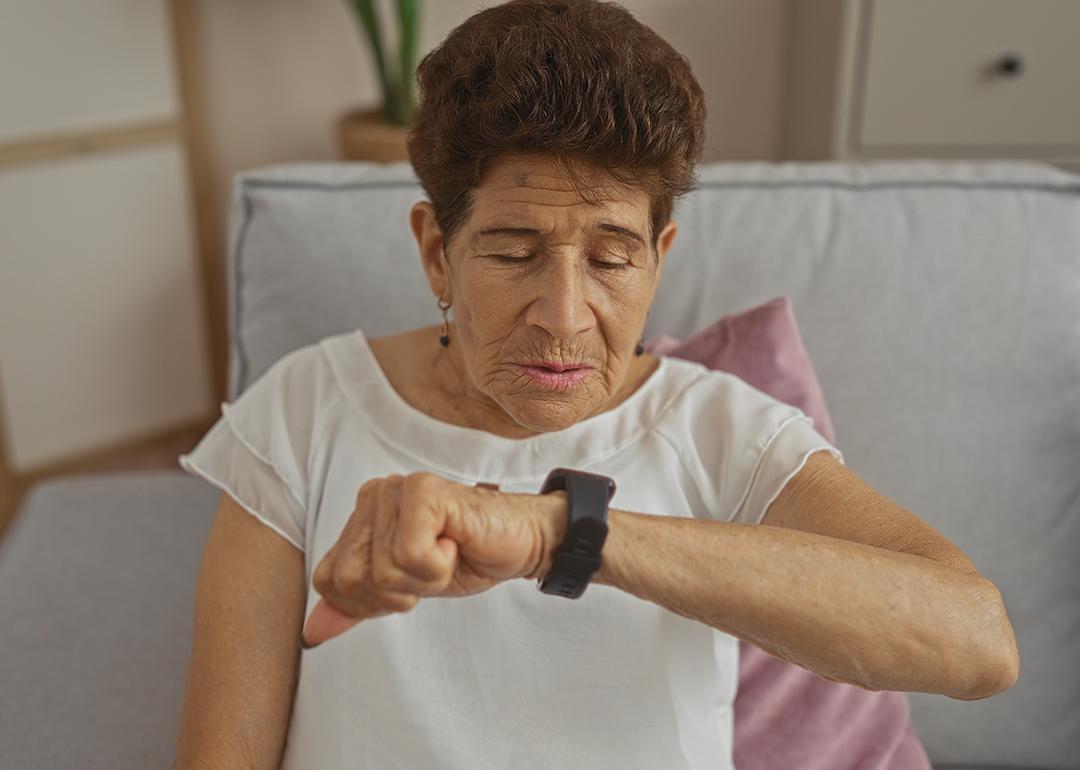 A senior woman observing her smartwatch while sitting on a sofa at home.