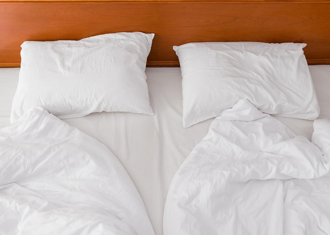 A view from above of an unmade bed with two duvets and white pillows.