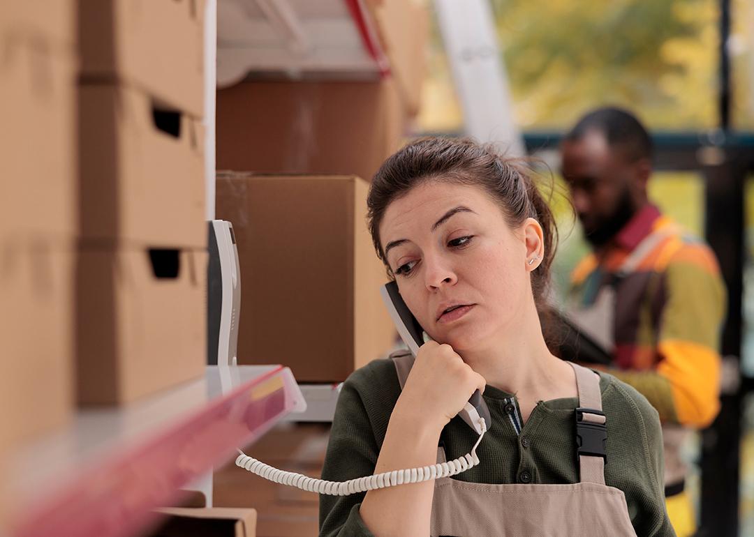 A warehouse worker talking over the landline phone about package shipment.