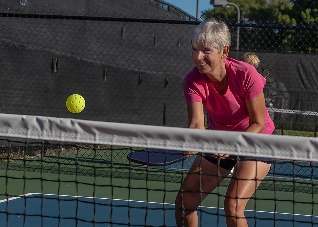 An elderly person enjoying a good time while playing pickleball in a court.