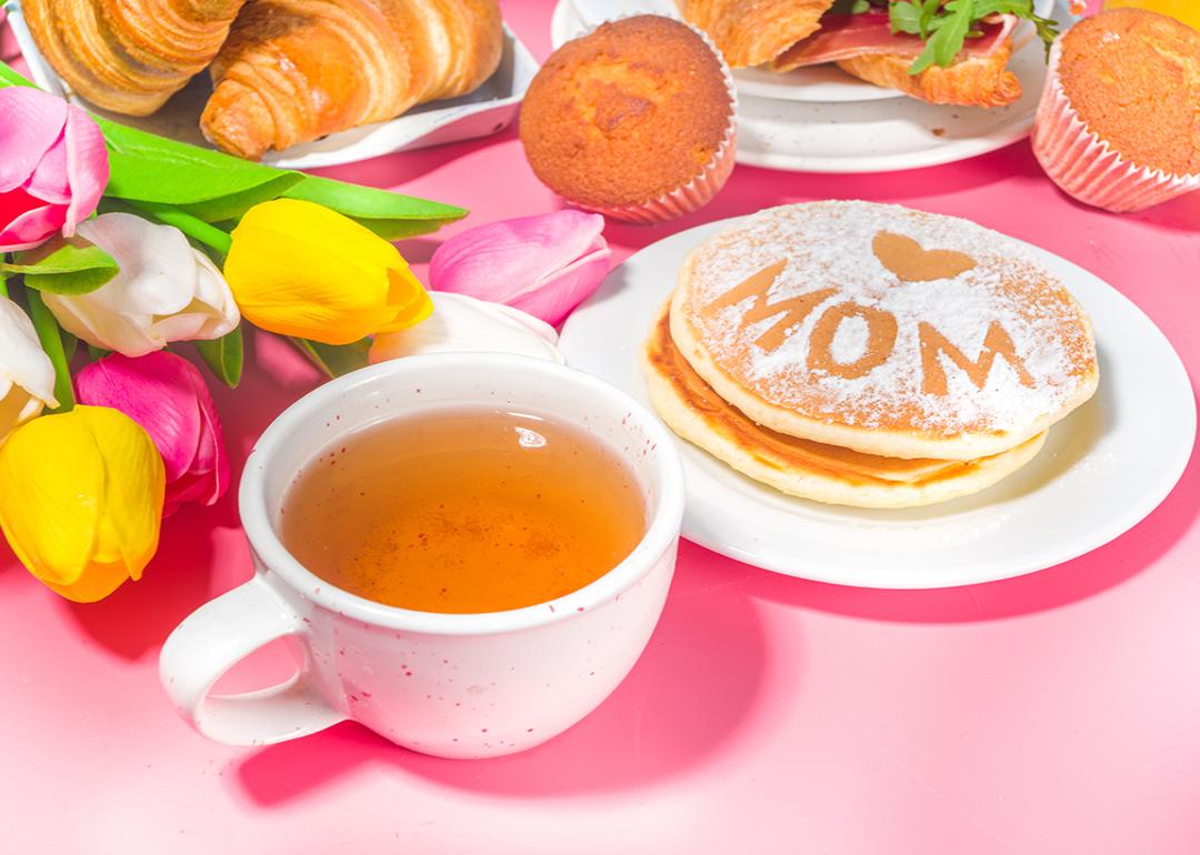 A pink-themed Mother's Day brunch meal featuring a bouquet of flowers, a cup of tea, and pancakes.