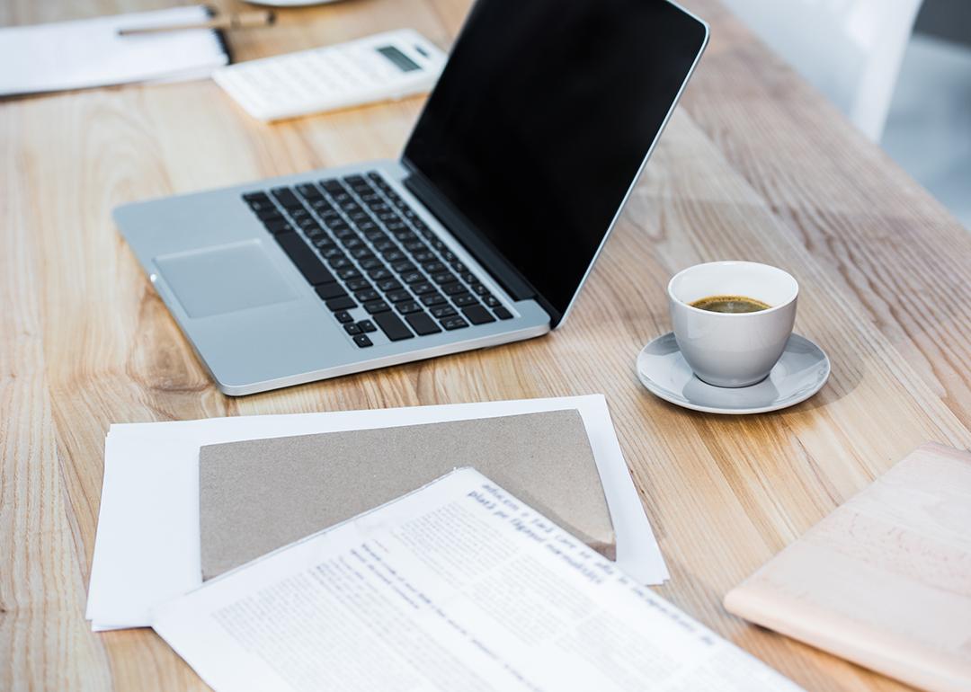 A workplace table with a laptop, coffee, and file documents.