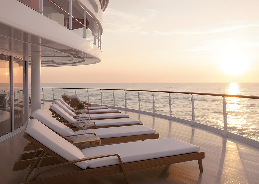 Lounge chairs on a ship deck facing the ocean's horizon during sunset.