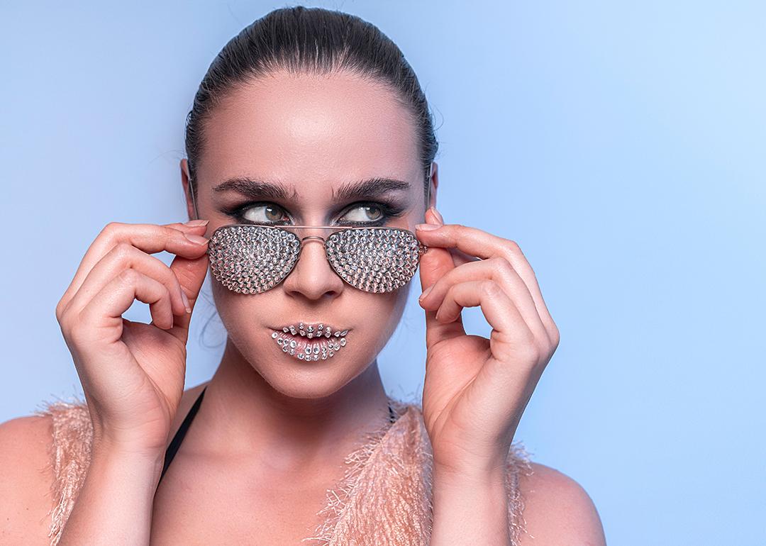 A female model wearing a rhinestone sunglasses and with rhinestones makeup on her lips.