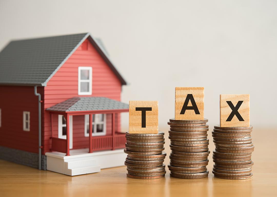 A miniature house and stacks of coins under TAX alphabet blocks.