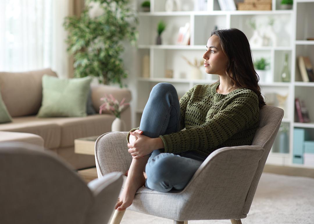 A woman sitting at home pensively looking out the window.