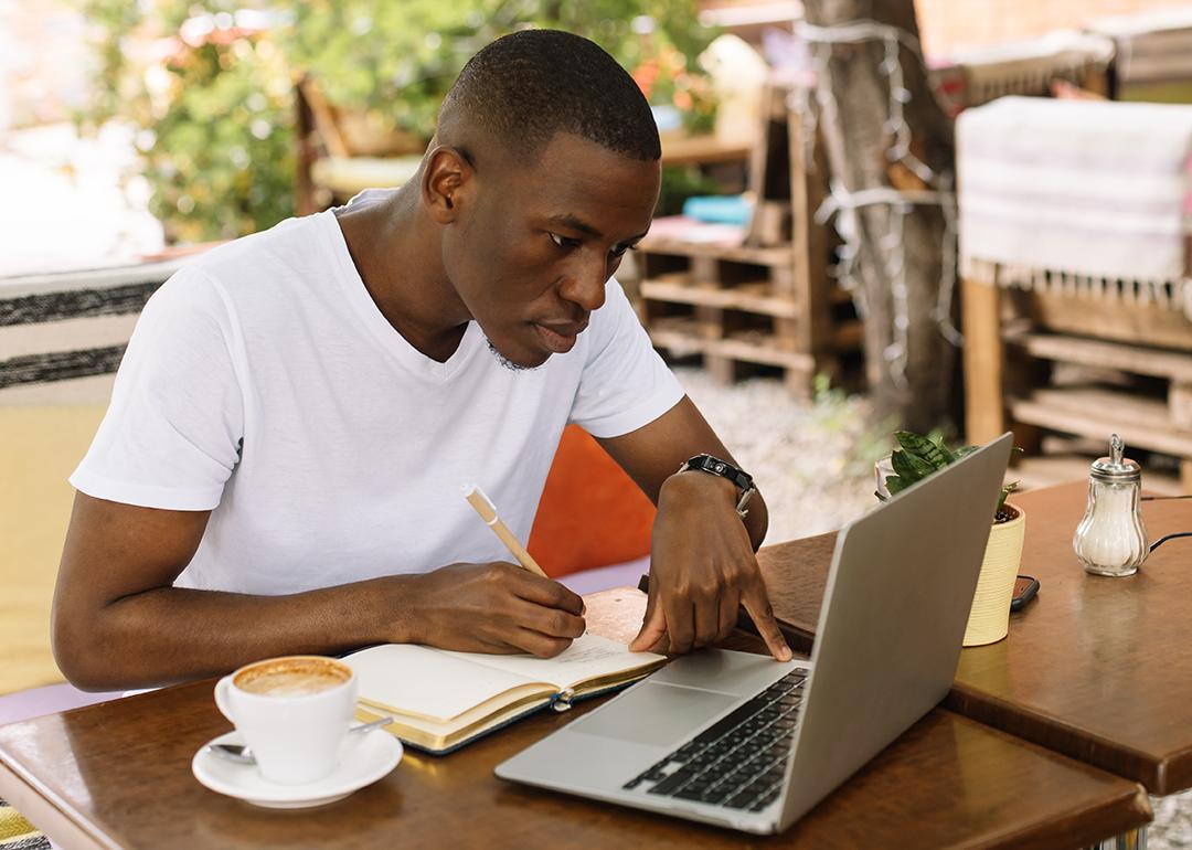 A young male student focused on working with a laptop in an outdoor cafe.